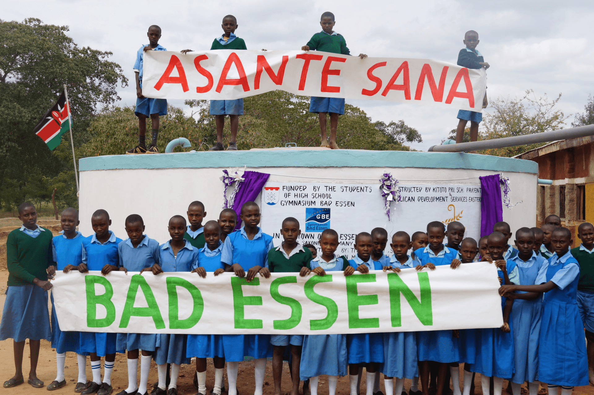 Children with an Asante Sana and Bad Essen banner in front of the water cistern