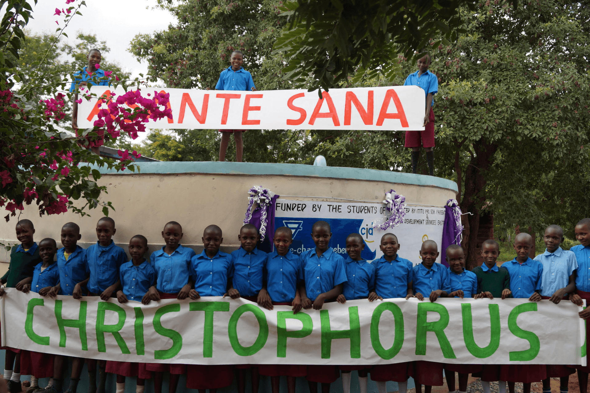 Children with an Asante Sana and Christophorusschule banner in front of the water cistern