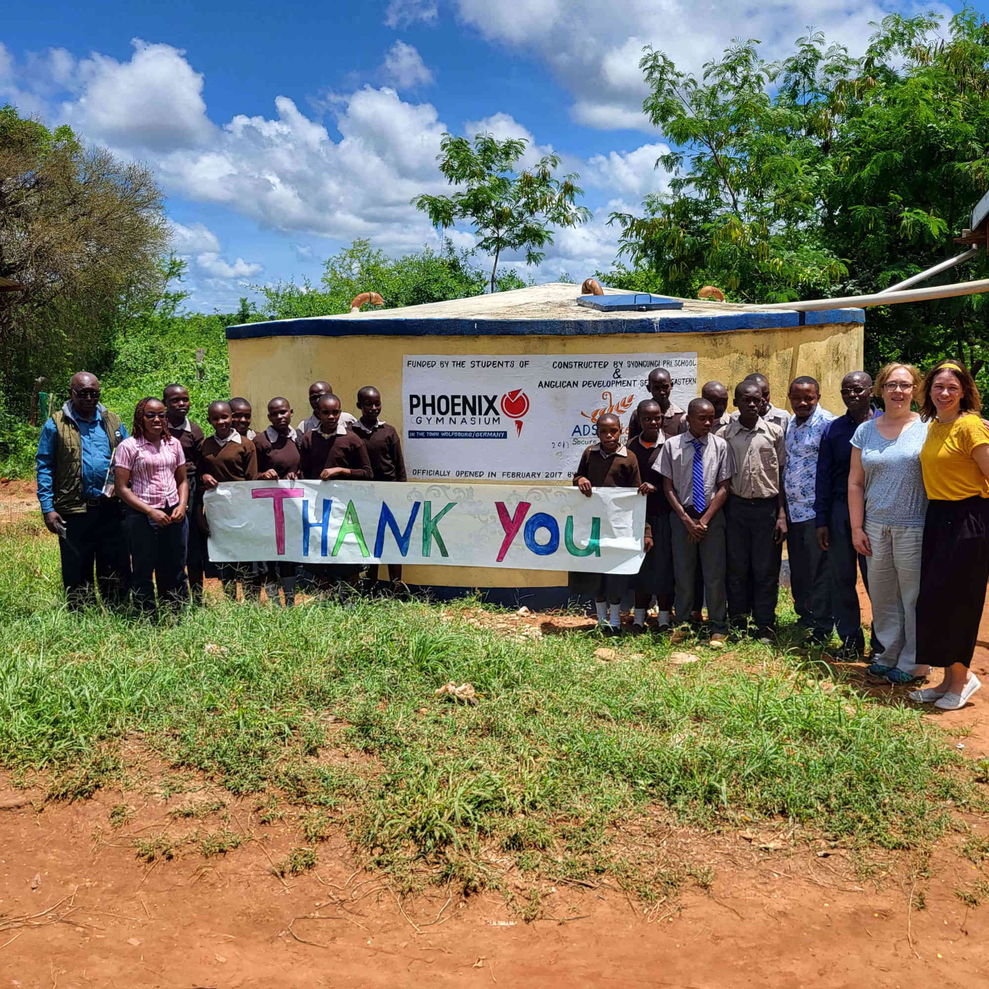 Students with a thank-you banner at the handover of the water tank in Syongungi