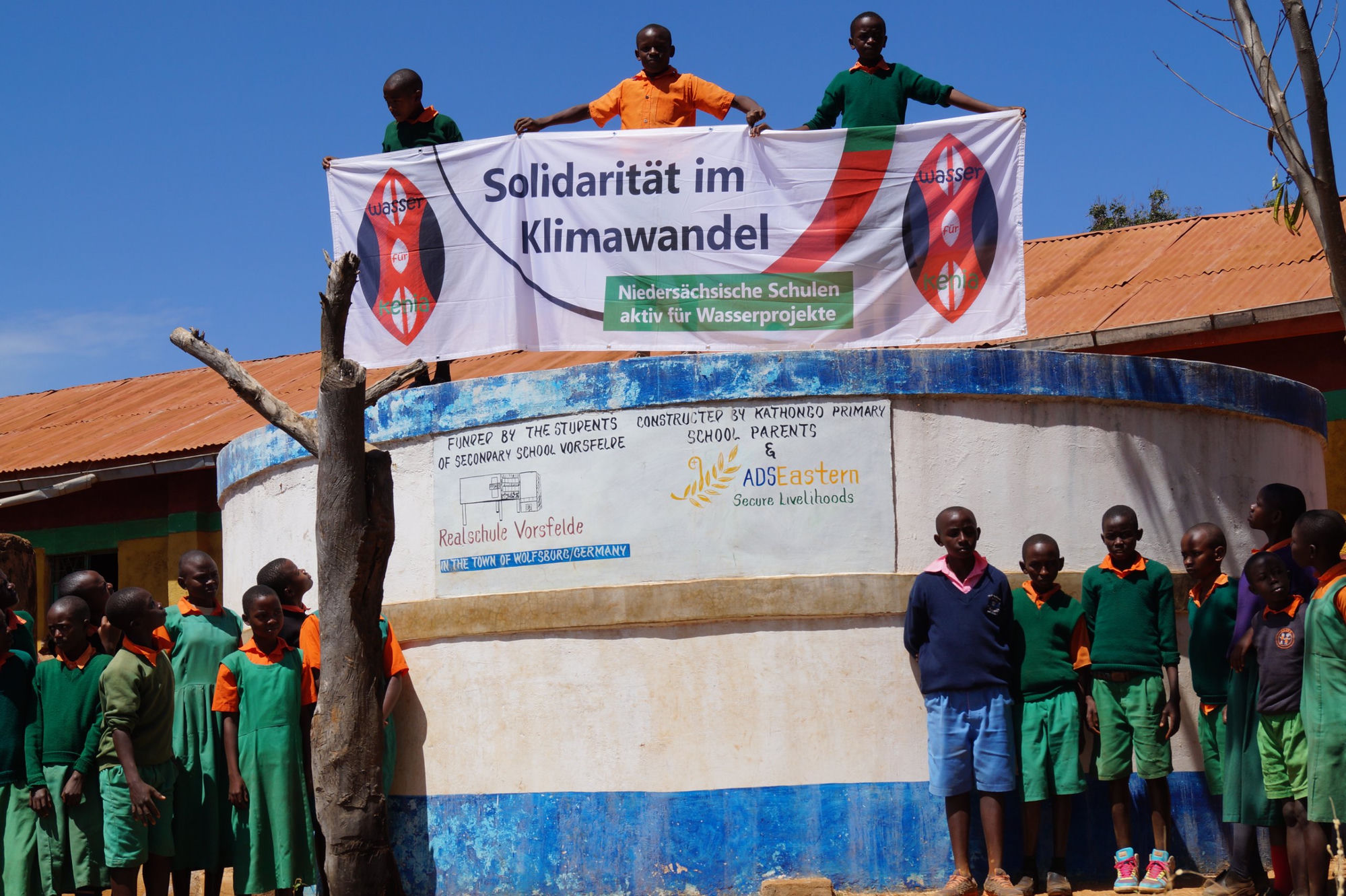 Schoolchildren with a solidarity banner on the water tank at Kathongo Primary School